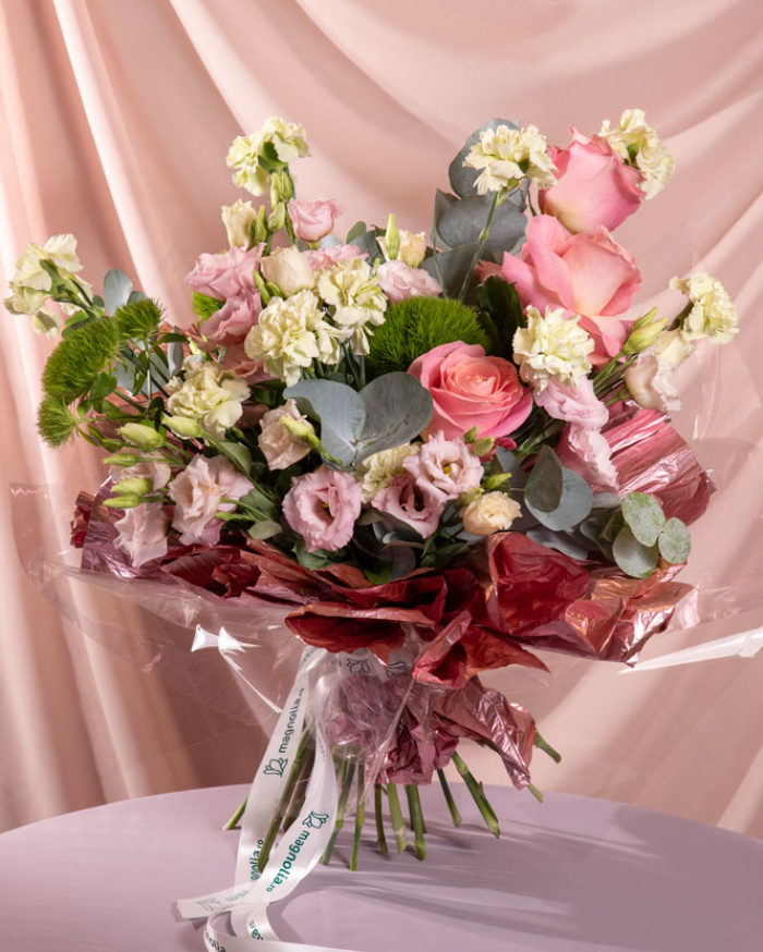 Perspectiva care evidentiaza proportiile si dimensiunea buchetului Duetul florilor, varianta Premium, o compozitie bogata alcatuita din 3 trandafiri roz, 10 garoafe verzi, 3 fire de lisianthus roz si 3 garoafe puf, finisata elegant cu 2 crengute de eucalipt, 2 crengute de ruscus mic, un ambalaj decorativ si 2 panglici.