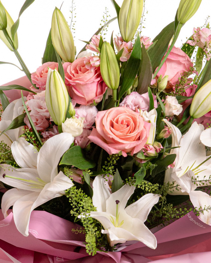 Prim-plan al florilor din buchetul "Pastel Beauty", varianta Premium, evidentiind combinatia armonioasa de 5 crini orientali albi, 6 trandafiri roz, 3 fire de lisianthus roz, 4 alstroemeria roz, completate de 4 fire de lepidium si finisate cu 2 ambalaje decorative si 2 panglici elegante.