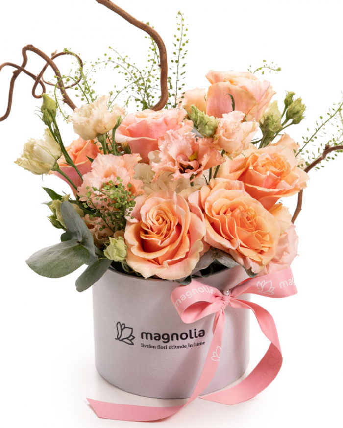 Imagine de ansamblu a aranjamentului “Aranjament delicat cu trandafiri si eustoma”, varianta Premium, realizat din 1 hortensie alba, 7 trandafiri portocalii, 2 fire de eustoma somon, 1 crenguta de lepidium si 1 crenguta de eucalipt, completat cu 1 crenguta de corylus, totul prezentat intr-o cutie alba Magnolia si o panglica roz eleganta.