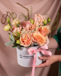 Perspectiva care evidentiaza proportiile si dimensiunea aranjamentului “Aranjament delicat cu trandafiri si eustoma”, varianta Premium, o compozitie bogata alcatuita din 1 hortensie alba, 7 trandafiri portocalii, 2 fire de eustoma somon si 1 crenguta de lepidium, completata cu eucalipt si crenguta de corylus, finisata elegant cu o cutie alba si o panglica roz.