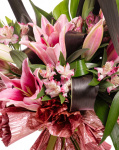 Prim-plan al florilor din buchetul “Buchet crini orientali”, varianta Premium, evidentiind combinatia armonioasa de 3 Crini orientali roz, 1 frunză de Monstera, 5 frunze de Cordiline, 4 flori de Alstroemeria, completate de 1 element decorativ și finisate cu o panglică neînscripționată elegantă.