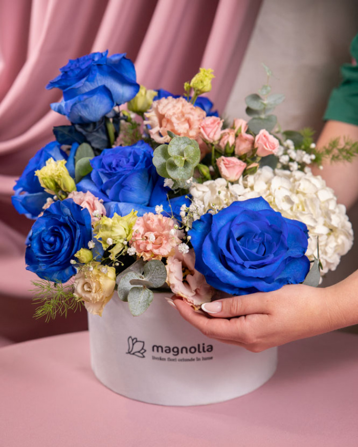 Perspectivă care evidențiază proporțiile și dimensiunea aranjamentului “Aranjament floral cu Trandafiri albaștri „Blue Dream””, varianta Premium, o compoziție bogată alcătuită din 7 Trandafiri albaștri, 1 Hortensie albă, 1 Eustoma somon, 1 Trandafir ramificat și 1 fir de Gypsophila, finisată elegant într-o cutie albă premium.