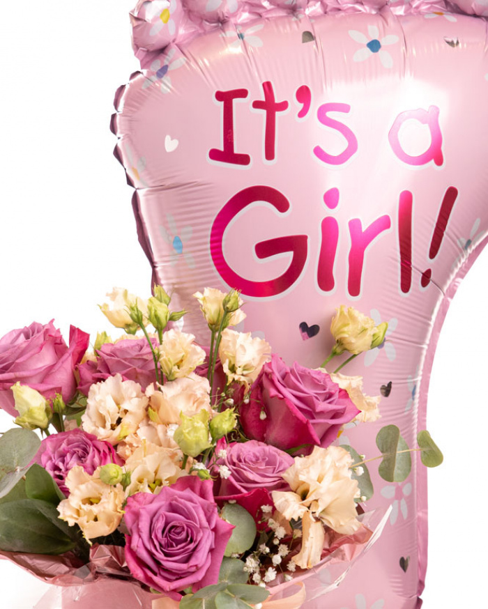 Prim-plan al florilor din aranjamentul “Aranjament floral „It'a a Girl””, varianta Premium, evidențiind combinația armonioasă de 7 Trandafiri mov, 1 fir de Gypsophila, 2 flori de Eustoma somon, completate de 2 crenguțe de Cinerea și finisate cu 1 panglică neinscripționată, 1 perlă cu ac, ambalaj decorativ și 1 balon roz.