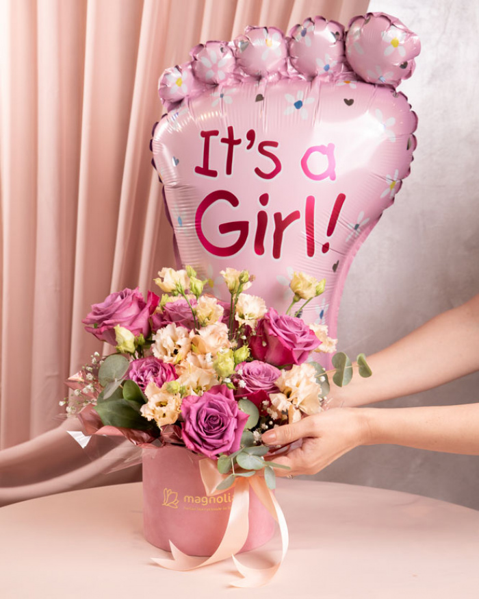 Perspectivă care evidențiază proporțiile și dimensiunea aranjamentului “Aranjament floral „It'a a Girl””, varianta Premium, o compoziție bogată alcătuită din 7 Trandafiri mov, 1 fir de Gypsophila, 2 flori de Eustoma somon, 2 crenguțe de Cinerea, finisată elegant cu 1 panglică neinscripționată, 1 perlă cu ac, ambalaj decorativ și 1 balon roz.