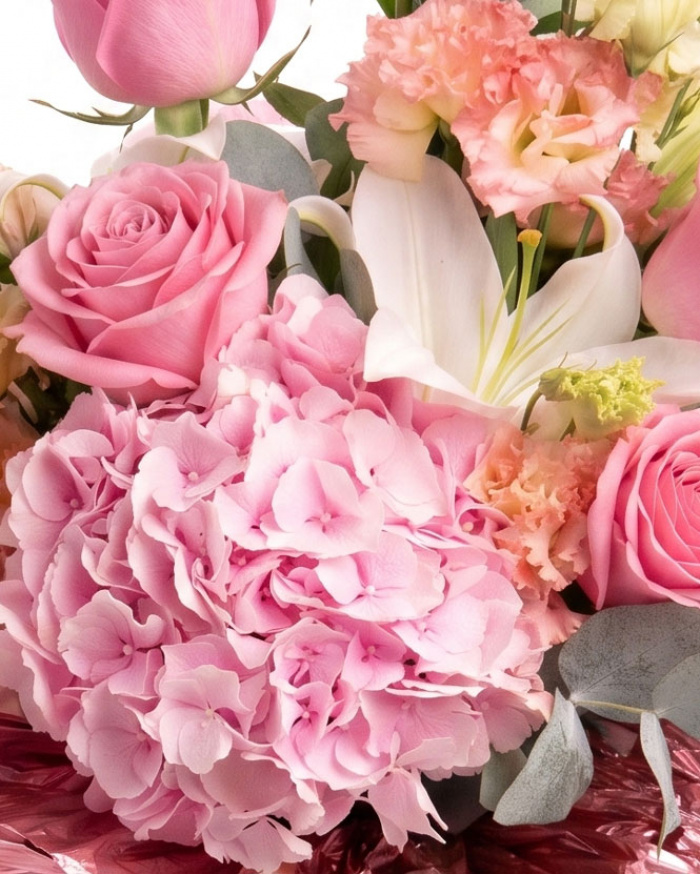 Prim-plan al florilor din buchetul “Buchet de flori „Bucurie de vară"”, varianta Deluxe, evidențiind combinația armonioasă de 1 Crin imperial alb, 2 fire de Eustoma somon, 1 Hydrangea roz, 1 fir de Trandafir ramificat roz și 5 Trandafiri roz, completate de crenguțe de Eucalipt și finisate cu o panglică elegantă.