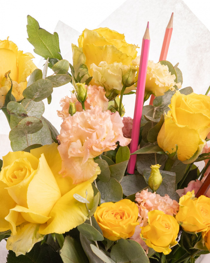 Prim-plan al florilor din buchetul “Buchet trandafiri galbeni și creioane colorate „Back to school"”, varianta Deluxe, evidențiind combinația armonioasă de 4 Trandafiri galbeni, 2 Eustoma somon, 1 Trandafir ramificat galben și 1 set de creioane colorate, completate de 2 crenguțe de Eucalipt și finisate cu 1 ambalaj și 1 panglică elegante.
