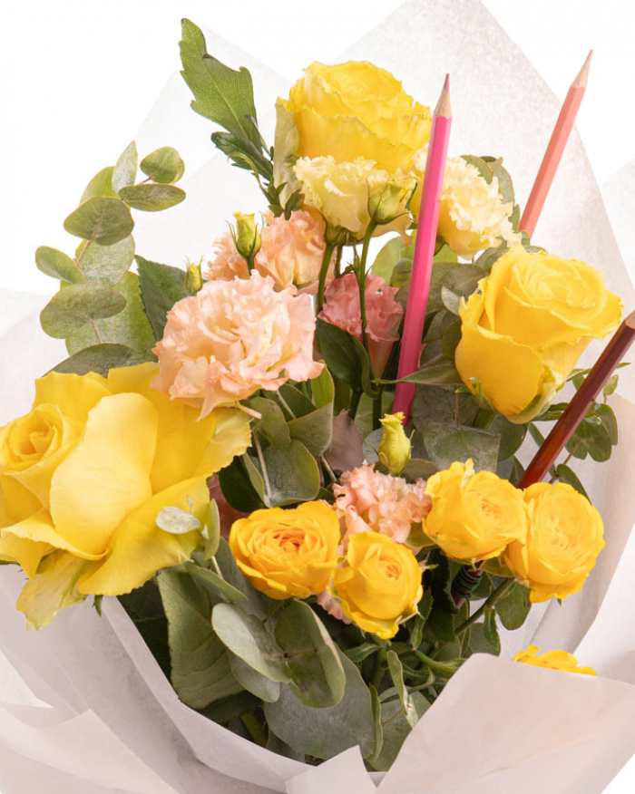 Prim-plan al florilor din buchetul “Buchet trandafiri galbeni și creioane colorate „Back to school"”, varianta Standard, evidențiind combinația armonioasă de 3 Trandafiri galbeni, 1 Eustoma somon, 1 Trandafir ramificat galben și 1 set de creioane colorate, completate de 2 crenguțe de Eucalipt și finisate cu 1 ambalaj și 1 panglică elegante.