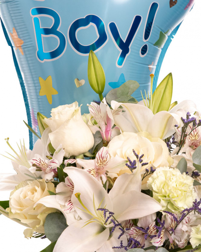 Prim-plan al florilor din aranjamentul “Aranjament floral „It'a a Boy””, varianta Deluxe, evidentiind combinatia armonioasa de 5 Trandafiri albi Mondial, 2 Crini imperiali albi, 3 Garoafe verzi, 3 Alstroemeria, 1 fir de Limonium, completate de 2 crenguțe de Eucalipt si finisate cu un balon festiv albastru, 1 perlă pe ac, cutie Magnolia și panglici elegante.