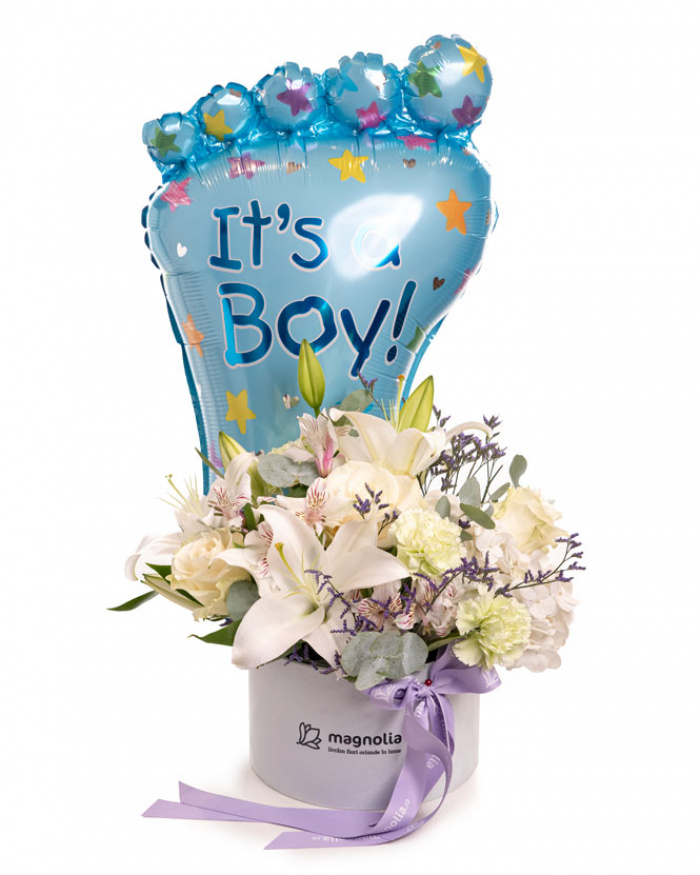 Imagine de ansamblu a aranjamentului “Aranjament floral „It'a a Boy””, varianta Standard, realizat din 3 Trandafiri albi Mondial, 2 Crini imperiali albi, 3 Garoafe verzi, 2 Alstroemeria, 1 fir de Limonium, 2 crenguțe de Eucalipt, completat cu un balon tematic It's a Boy, 1 perlă decorativă pe ac, o cutie Magnolia și panglică personalizată.