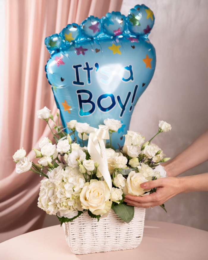 Perspectiva care evidentiaza proportiile si dimensiunea coșului “Coș cu flori nou-născut „Welcome Baby Boy””, varianta Premium, o compozitie bogata alcatuita din 2 Hydrangea albe, 5 Trandafiri albi, 3 fire de Eustoma albă, 3 Trandafiri ramificați albi, 1 Limonium mic, 2 fire de Asparagus umbelatus, finisata elegant cu un coș alb, o panglică și un balon festiv.
