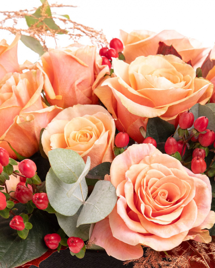 Prim-plan al florilor din cutia “Cutie de toamnă cu trandafiri și hypericum”, varianta Premium, evidentiind combinatia armonioasa de 9 Trandafiri portocalii și 2 ramuri de Hypericum, completate de verdeață de Quercus, Asparagus coloured și Eucalipt și finisate cu o cutie rotundă neagră elegantă.