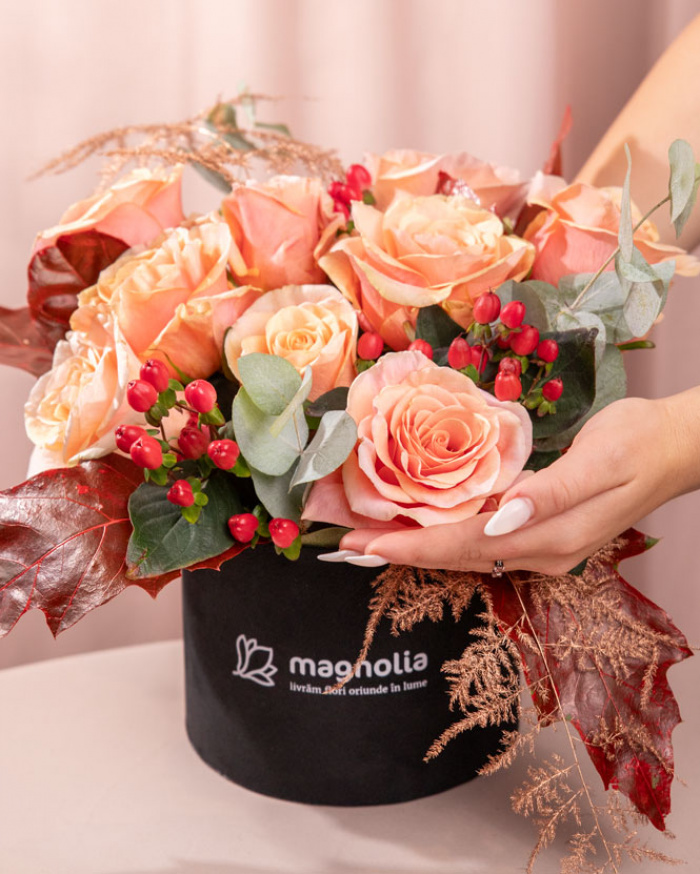 Perspectiva care evidentiaza proportiile si dimensiunea cutiei “Cutie de toamnă cu trandafiri și hypericum”, varianta Premium, o compozitie bogata alcatuita din 9 Trandafiri portocalii, 2 ramuri de Hypericum, 1 crenguță de Quercus, 2 fire de Asparagus coloured și 1 crenguță de Eucalipt, finisata elegant cu o cutie rotundă neagră.