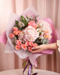 Perspectivă care evidențiază proporțiile și dimensiunea buchetului “Buchet cu hortensii „Pink Dream””, varianta Premium, o compoziție bogată alcătuită din 5 Trandafiri ramificați roz, 2 Hydrangee roz, 3 Alstroemeria, 2 crenguțe de Eucalipt, finisată elegant cu ambalaj decorativ și 2 panglici Magnolia.