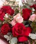 Prim-plan al florilor din buchetul “Buchet cu trandafiri roșii „Rose Whisper””, varianta Premium, evidentiind combinatia armonioasa de 7 Trandafiri roșii, 3 Trandafiri ramificați roz, 3 fire de Chamelaucium roz și 2 fire de Symphoricarpos, completate de 3 crenguțe de Eucalipt si finisate cu 2 ambalaje decorative și o panglică Magnolia elegante.