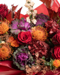 Prim-plan al florilor din buchetul “Buchet de toamnă „Exotic Love””, varianta Premium, evidențiind combinația armonioasă de 5 Trandafiri roșii, 3 Leucospermum, 3 Brassica, 3 Carthamus, 2 Hydrangea burgundy, 1 Trandafir ramificat portocaliu și 2 Symphoricarpos, completate de 3 fire de Asparagus cupru și 3 crenguțe de Quercus și finisate cu ambalaj decorativ și o panglică Magnolia elegante.