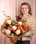 Perspectiva care evidențiază proporțiile și dimensiunea buchetului “Buchet colorat de toamna”, varianta Premium, o compoziție bogată alcătuită din 5 Trandafiri albi, 2 crenguțe de Symphoricarpos, 2 fire de Carthamus, 3 Trandafiri ramificați portocalii, 3 Trandafiri ramificați roșii, 2 frunze de Quercus, 1 crenguță de Eucalipt, finisată elegant cu ambalaj decorativ și o panglică Magnolia.