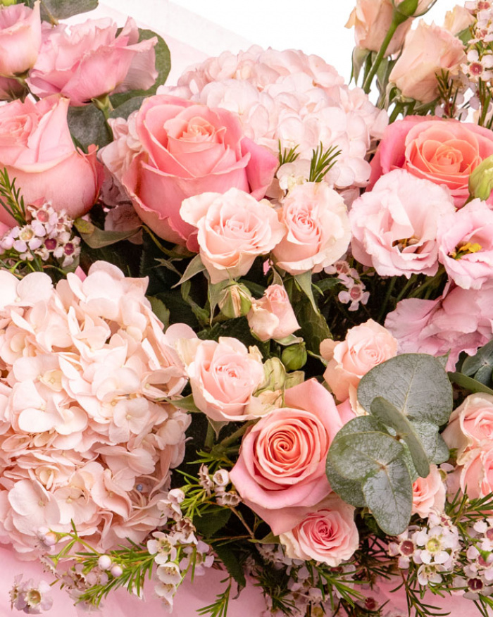 Prim-plan al florilor din buchetul “Buchet luxuriant cu flori roz”, varianta Premium, evidentiind combinatia armonioasa de 2 Hortensii roz, 5 Trandafiri roz, 4 Trandafiri ramificați roz, 4 fire de Chamelaucium roz și 2 fire de Eustoma roz, completate de 3 crenguțe de Eucalipt si finisate cu 2 ambalaje decorative și o panglică Magnolia elegante.