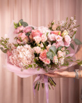 Perspectiva care evidentiaza proportiile si dimensiunea buchetului “Buchet luxuriant cu flori roz”, varianta Premium, o compozitie bogata alcatuita din 2 Hortensii roz, 5 Trandafiri roz, 4 Trandafiri ramificați roz, 4 fire de Chamelaucium roz, 2 fire de Eustoma roz și 3 crenguțe de Eucalipt, finisata elegant cu 2 ambalaje decorative și o panglică Magnolia.