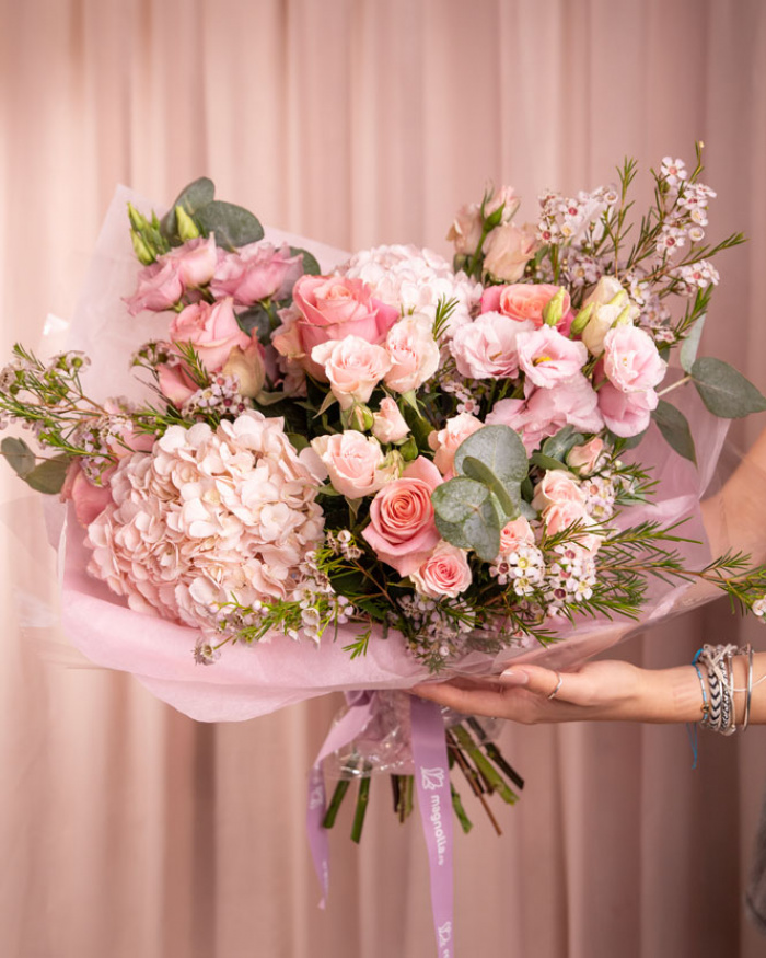 Perspectiva care evidentiaza proportiile si dimensiunea buchetului “Buchet luxuriant cu flori roz”, varianta Premium, o compozitie bogata alcatuita din 2 Hortensii roz, 5 Trandafiri roz, 4 Trandafiri ramificați roz, 4 fire de Chamelaucium roz, 2 fire de Eustoma roz și 3 crenguțe de Eucalipt, finisata elegant cu 2 ambalaje decorative și o panglică Magnolia.