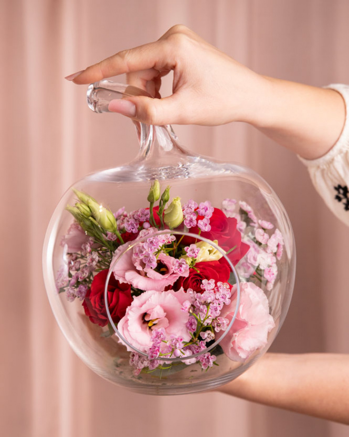 Prim-plan al florilor din aranjamentul “Aranjament floral în vas decorativ „Pink & Red””, varianta Standard, evidențiind combinația armonioasă de 1 fir de Eustoma roz, 1 fir de Trandafir ramificat roșu și 1 fir de Chamelaucium roz, completate de accente proaspete și finisate cu un măr de sticlă decorativ.