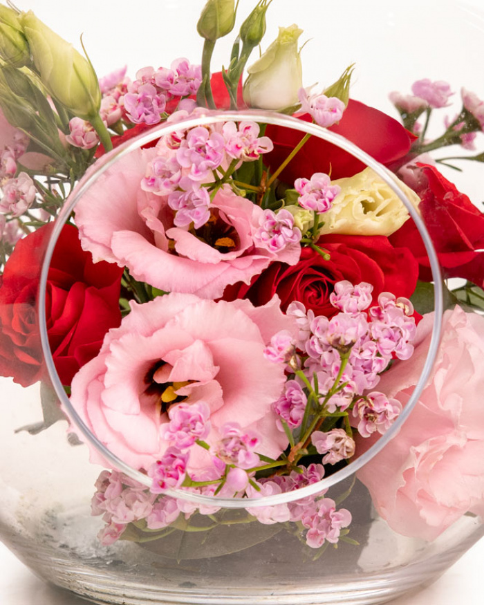 Prim-plan al florilor din aranjamentul “Aranjament floral în vas decorativ „Pink & Red””, varianta Standard, evidențiind combinația armonioasă de 1 fir de Eustoma roz, 1 fir de Trandafir ramificat roșu și 1 fir de Chamelaucium roz, completate de accente proaspete și finisate cu un măr de sticlă decorativ.