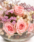 Prim-plan al florilor din aranjamentul floral “Aranjament floral „Blush Apple””, varianta Standard, evidentiind combinatia armonioasa de un fir de Trandafir ramificat roz, o crenguță de Chamelaucium roz și o crenguță de Symphoricarpos, completate de Eucalipt și Asparagus colorat și finisate cu un vas decorativ din sticlă în formă de măr.