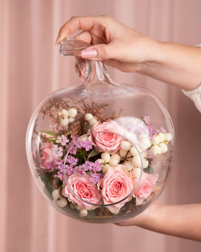 Imagine de ansamblu a aranjamentului floral “Aranjament floral „Blush Apple””, varianta Standard, realizat dintr-un fir de Trandafir ramificat roz, o crenguță de Chamelaucium roz, o crenguță de Symphoricarpos, o crenguță de Eucalipt și un fir de Asparagus colorat, completat cu un vas din sticlă în formă de măr.