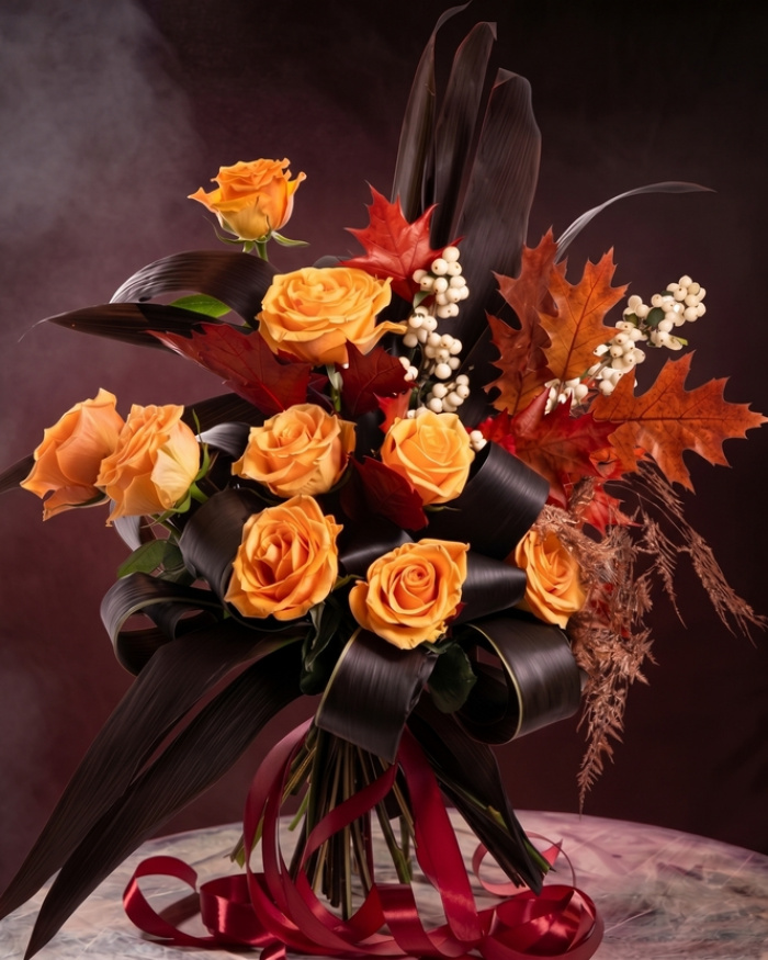 Perspectiva care evidentiaza proportiile si dimensiunea buchetului “Buchet de Halloween cu trandafiri”, varianta Premium, o compozitie bogata alcatuita din 9 Trandafiri portocalii, 13 frunze de Cordiline, 4 frunze de Quercus, 2 crenguțe de Asparagus cupru, 2 fire de Sumphoricarpus, finisata elegant cu 3 panglici.